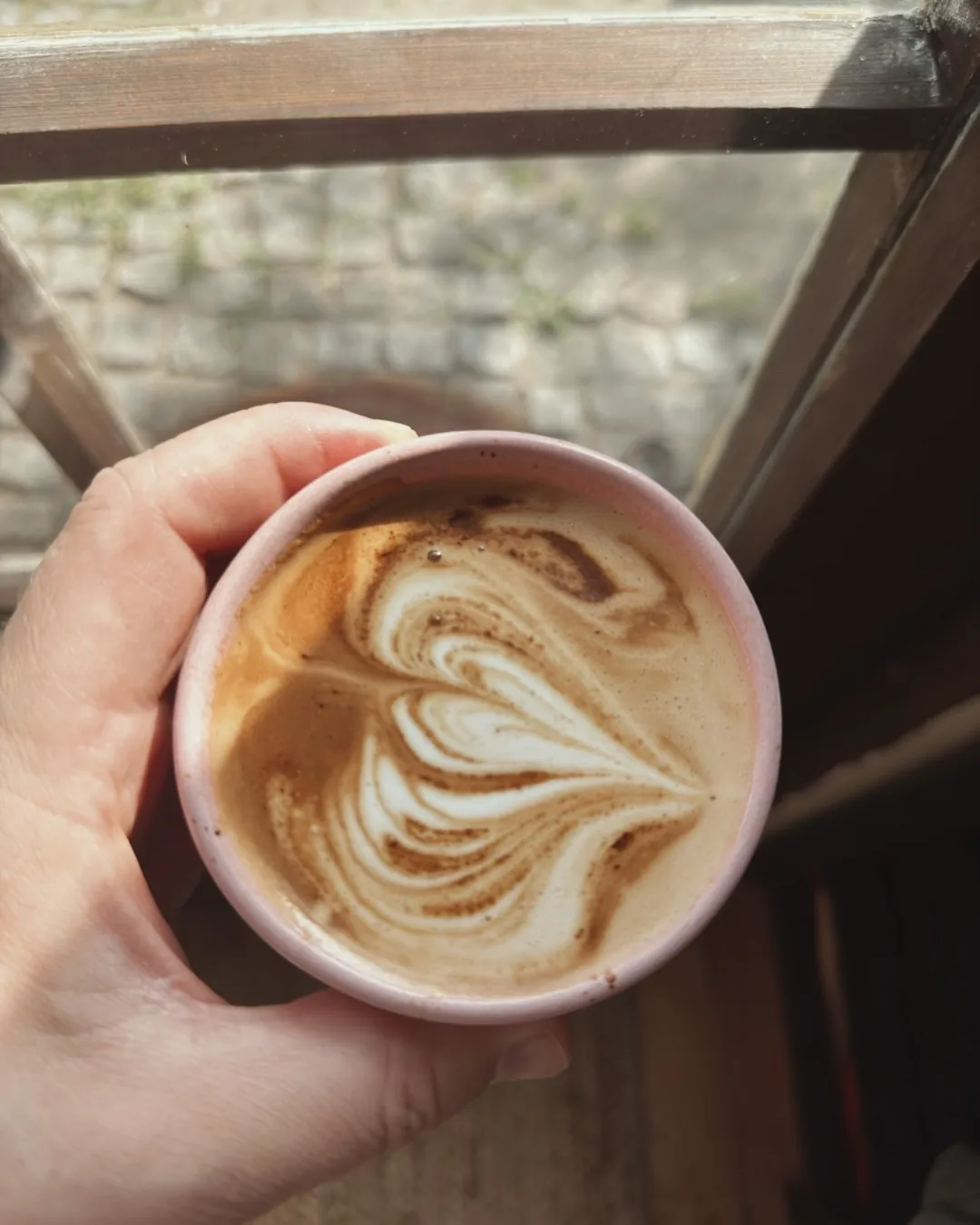Cappuccino in einer rosa Tasse, von oben, am Fenster